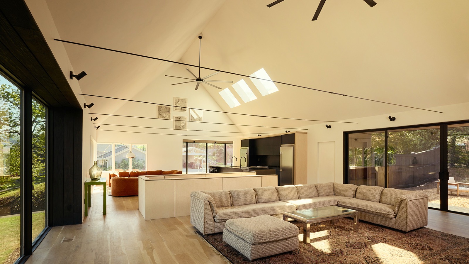 Interior of the Armstead Residence in Birmingham, Alabama — an open-plan living room and kitchen under a vaulted white ceiling with skylights, opening to the yard through black-framed glass doors